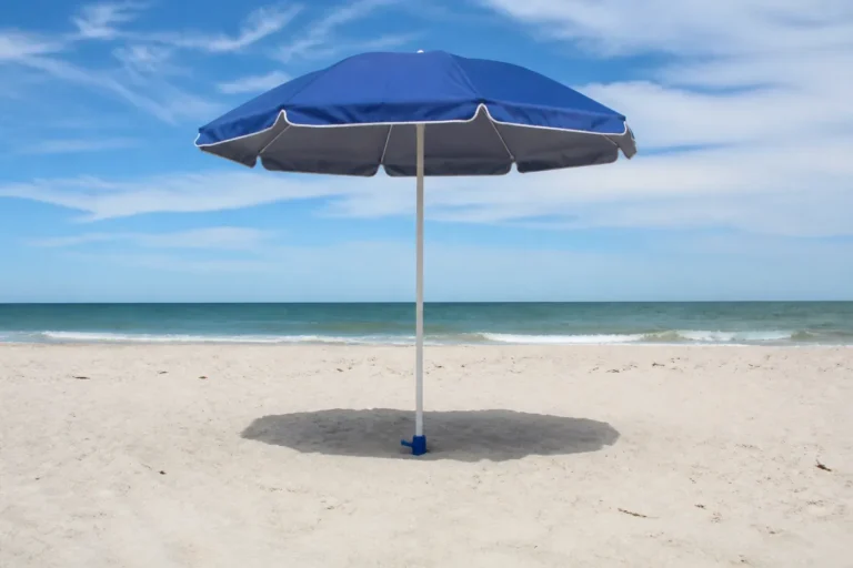 Blue beach umbrella installed in firm sand with only the top of a screw-in anchor visible