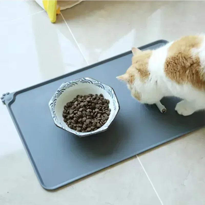 Gray silicone pet feeding mat under a food bowl with a cat beside it